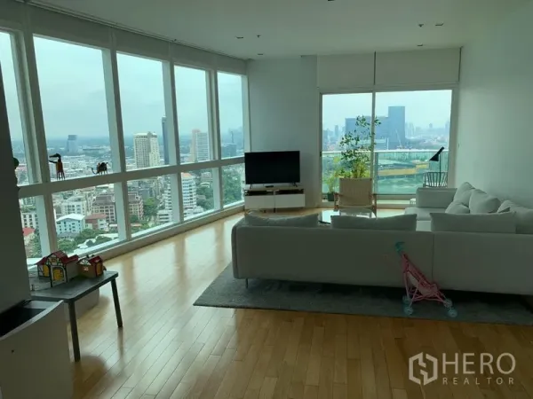 คอนโด ให้เช่าในKhlong Toei, Bangkok - ห้องนั่งเล่นมุมกระจกเต็มผนัง พื้นไม้ สีสว่าง พร้อมวิวสกายไลน์กรุงเทพฯ