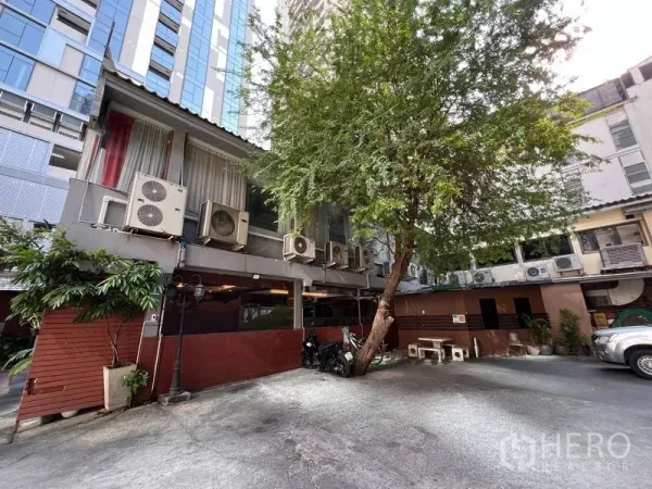 零售空间 出租或出售在Khlong Toei, Bangkok - 庭院与停车位，低层商铺外立面、成排空调机与大树，位于曼谷空堤区。