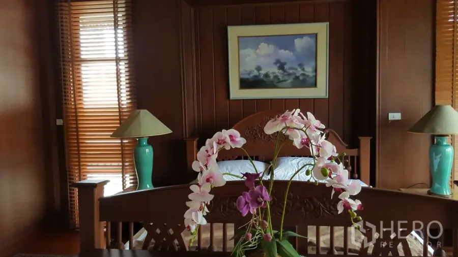 บ้าน ให้เช่าในKhlong Toei, Bangkok - ห้องนอนโทนไม้สัก อ่างเตียงแกะสลัก โคมไฟข้างเตียง ม่านบังตา และแจกันกล้วยไม้.