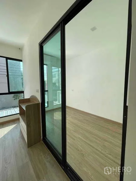 Townhouse for rent or sale in Bang Kapi, Bangkok - Hallway with black-framed sliding glass doors opening to a sunlit room with wood floors.