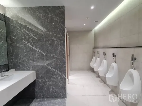 Office Space for rent - Modern men’s restroom with a marble accent wall, long white vanity and a row of urinals in an office building.