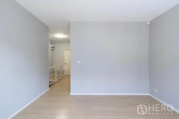 Townhouse for rent or sale in Watthana, Bangkok - Empty upper-level room with grey walls and wood laminate flooring.