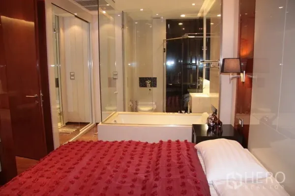 คอนโด ให้เช่าในKhlong Toei, Bangkok - ห้องนอนผ้าห่มสีแดงเชื่อมกับห้องน้ำผนังกระจก มีอ่างอาบน้ำและห้องอาบน้ำฝักบัว