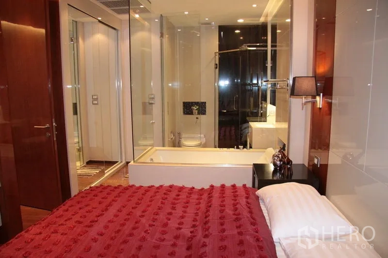 คอนโด ให้เช่าในKhlong Toei, Bangkok - ห้องนอนผ้าห่มสีแดงเชื่อมกับห้องน้ำผนังกระจก มีอ่างอาบน้ำและห้องอาบน้ำฝักบัว