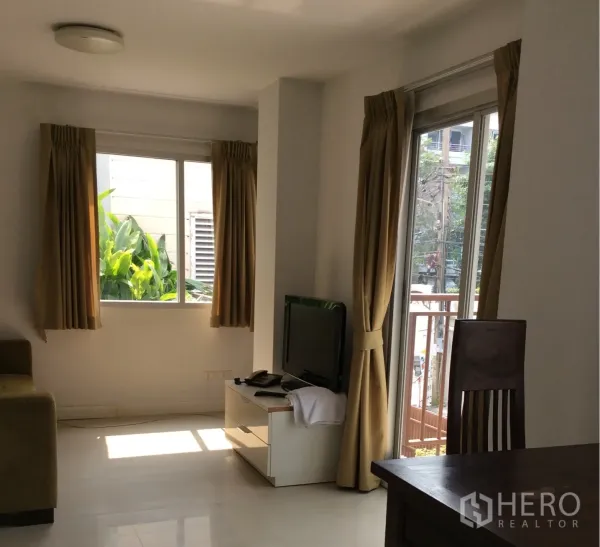 คอนโด ขายในPathum Wan, Bangkok - ห้องนั่งเล่นสว่างในคอนโดปทุมวัน มีชั้นวางทีวี โซฟา และประตูกระจกพร้อมผ้าม่านสีครีม