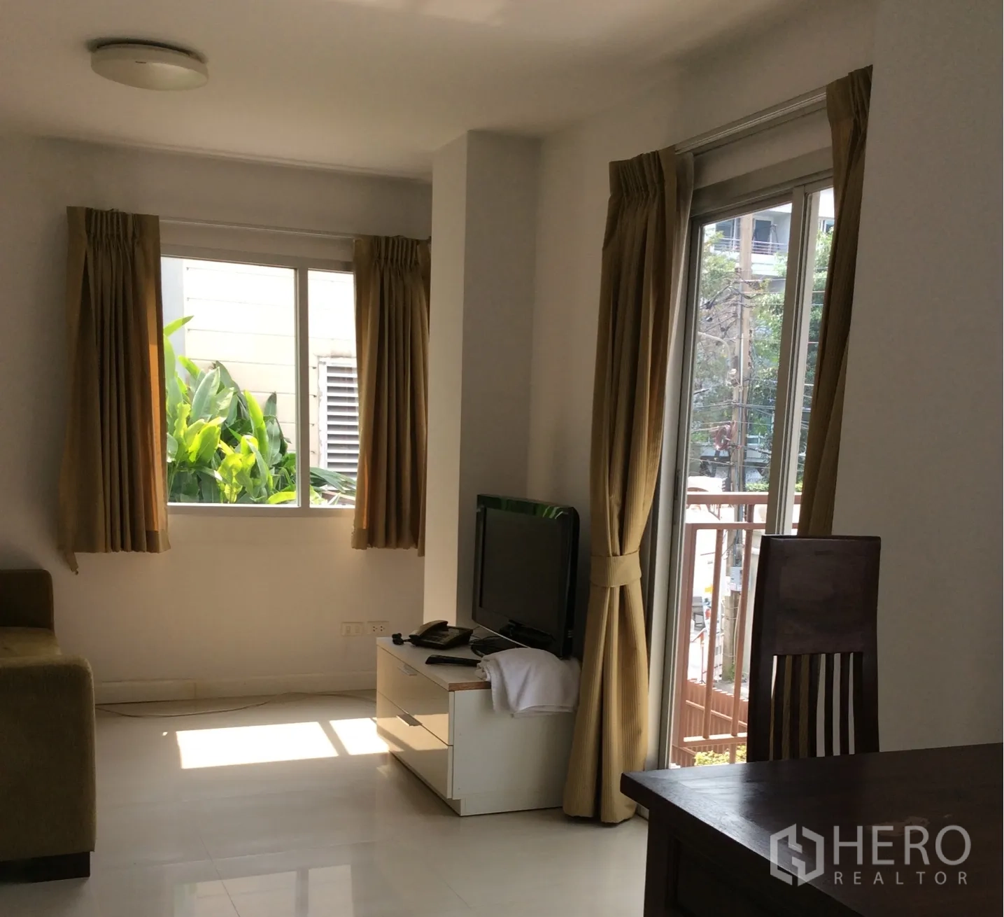 คอนโด ขายในPathum Wan, Bangkok - ห้องนั่งเล่นสว่างในคอนโดปทุมวัน มีชั้นวางทีวี โซฟา และประตูกระจกพร้อมผ้าม่านสีครีม