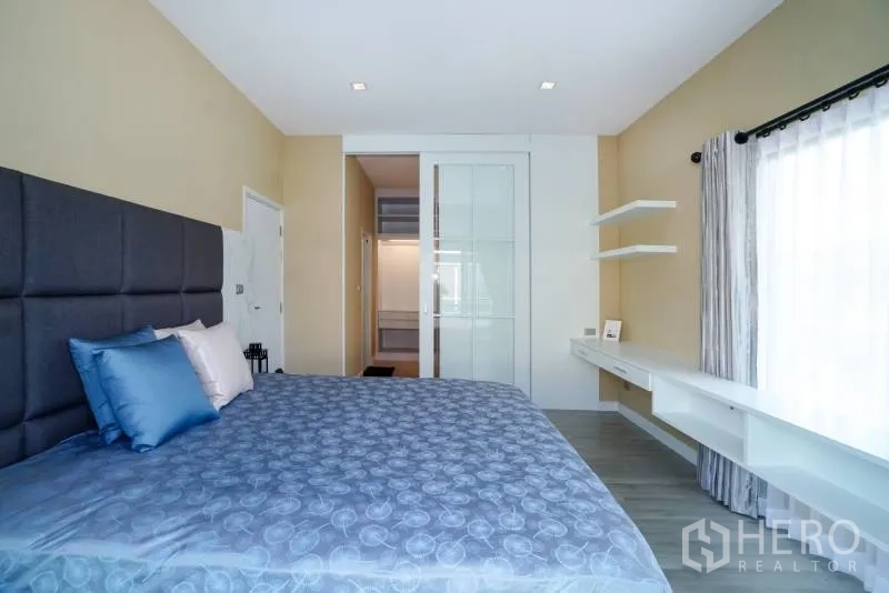 บ้าน ให้เช่าหรือขายในLat Krabang, Bangkok - ห้องนอนสว่างพร้อมหัวเตียงบุผ้า โต๊ะบิวท์อิน และประตูกระจกเลื่อนเข้าสู่ตู้เสื้อผ้า