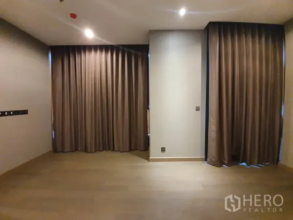 Condominium for rent in Huai Khwang, Bangkok - Spacious living area with wood flooring, recessed lighting, and full-height blackout curtains.