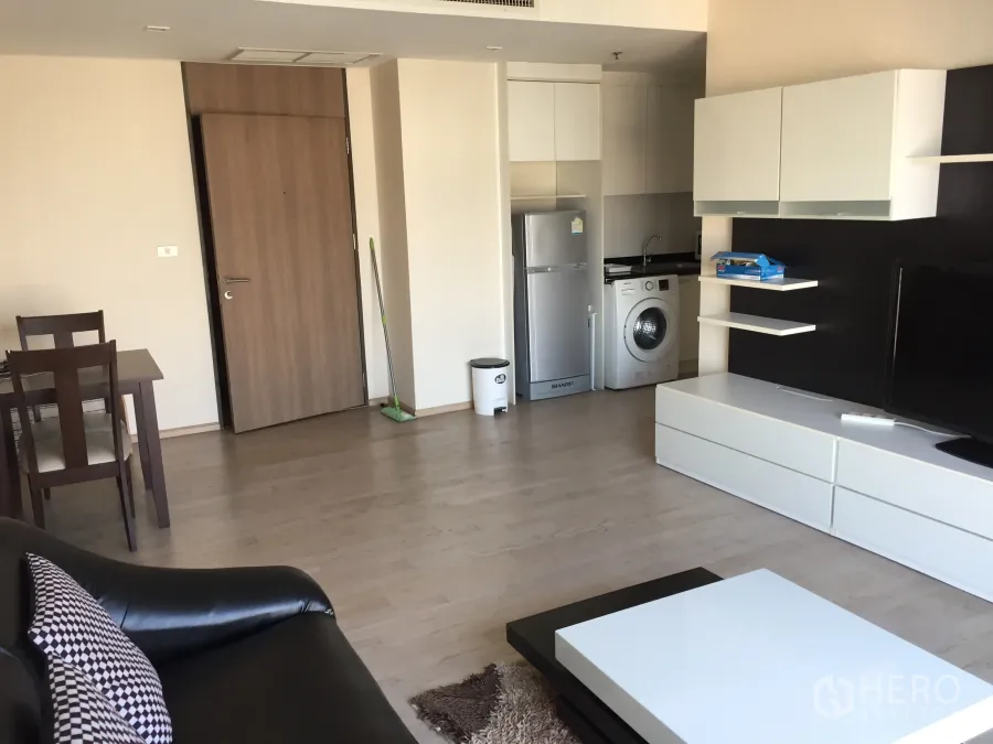 公寓 出租或出售在Khlong Toei, Bangkok - 开放式客厅，配餐桌、电视柜与小型厨房，带冰箱与洗衣机。