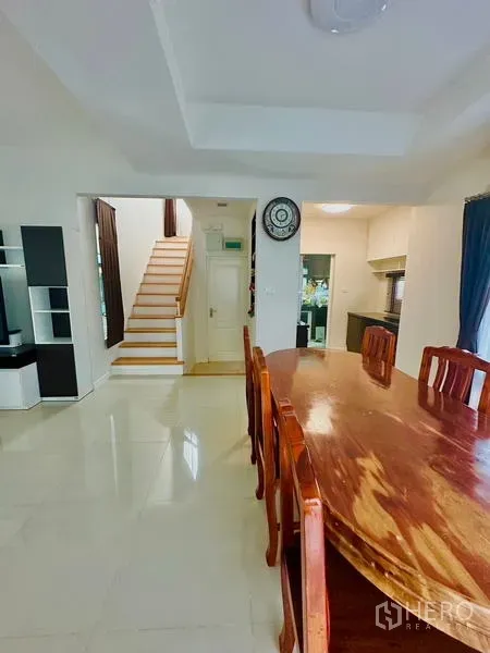 Detached House for sale in Prawet, Bangkok - Open dining area with glossy tile flooring, wooden table set and stairs to the upper floor.