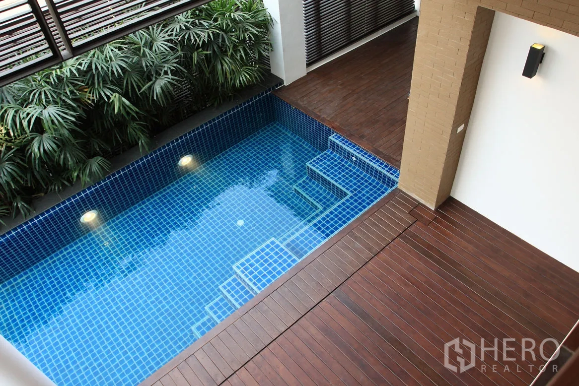 Detached House for rent in Khlong Toei, Bangkok - Private blue-tiled plunge pool with underwater lights beside a wooden deck and tropical plants.