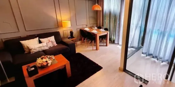Condominium for rent in Phra Khanong, Bangkok - Cozy lounge with sofa and dining table beside large curtained windows.