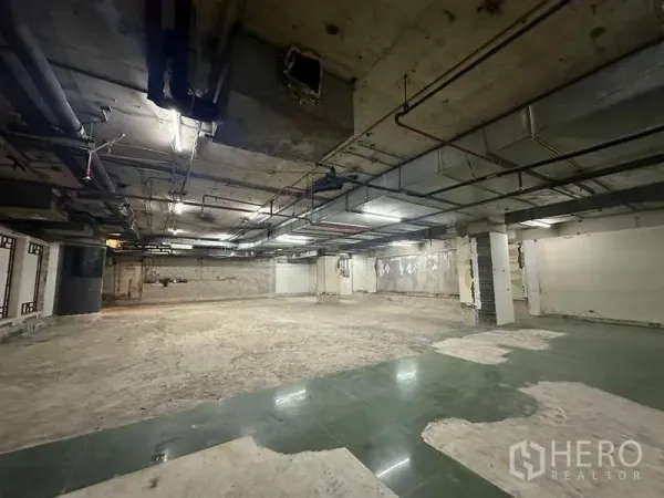 零售空间 出租 - 未装修的大型零售空间，外露风管与立柱，局部绿砖地面与日光灯。