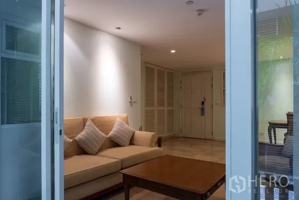 Apartment for rent in Bang Rak, Bangkok - Cozy living room viewed from sliding balcony doors with beige sofa, cushions, wooden coffee table and built-in storage.