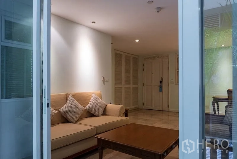 Apartment for rent in Bang Rak, Bangkok - Cozy living room viewed from sliding balcony doors with beige sofa, cushions, wooden coffee table and built-in storage.