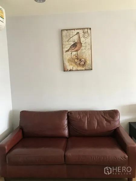 Condominium for rent in Watthana, Bangkok - Brown leather sofa against a light wall with framed artwork above.