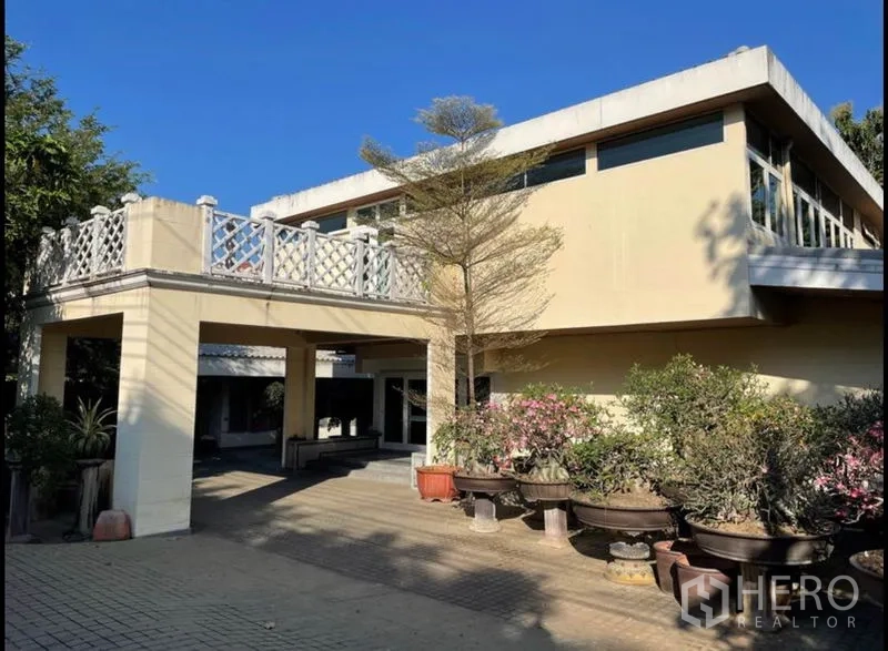 Detached House for rent in Khlong Toei, Bangkok - Two-storey cream detached house with large terrace and potted plants in the front courtyard.