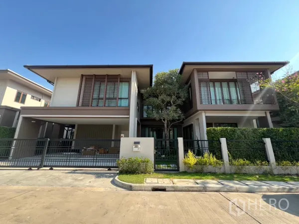 Detached House for rent or sale in Bang Kapi, Bangkok - Modern two-storey detached house with gated driveway and landscaped hedges under a clear sky.