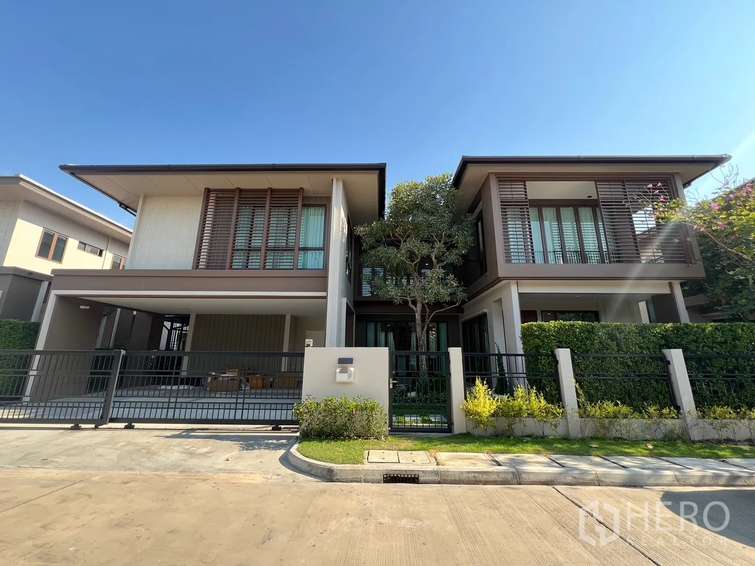 Detached House for rent or sale in Bang Kapi, Bangkok - Modern two-storey detached house with gated driveway and landscaped hedges under a clear sky.