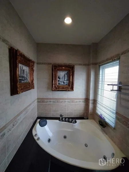 Detached House for sale in Phra Samut Chedi, Samut Prakan - Bathroom with corner jacuzzi bathtub, tiled walls, framed artwork and a window with blinds.