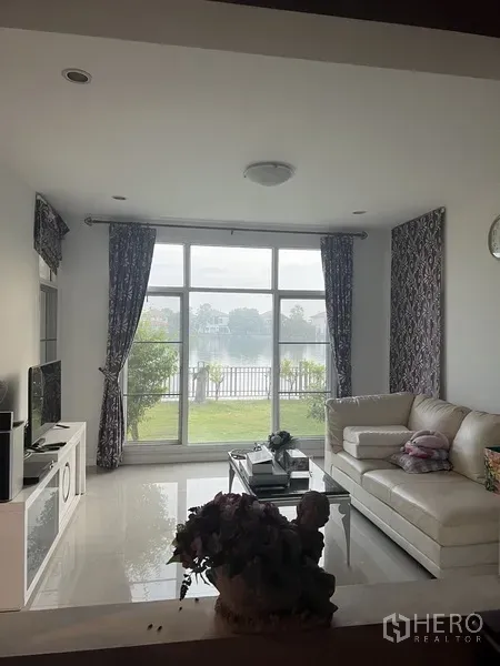 บ้าน ให้เช่าหรือขายในLat Krabang, Bangkok - ห้องนั่งเล่นสว่าง โซฟาสีขาว กระจกบานเต็มสูงชมวิวทะเลสาบที่เงียบสงบ.