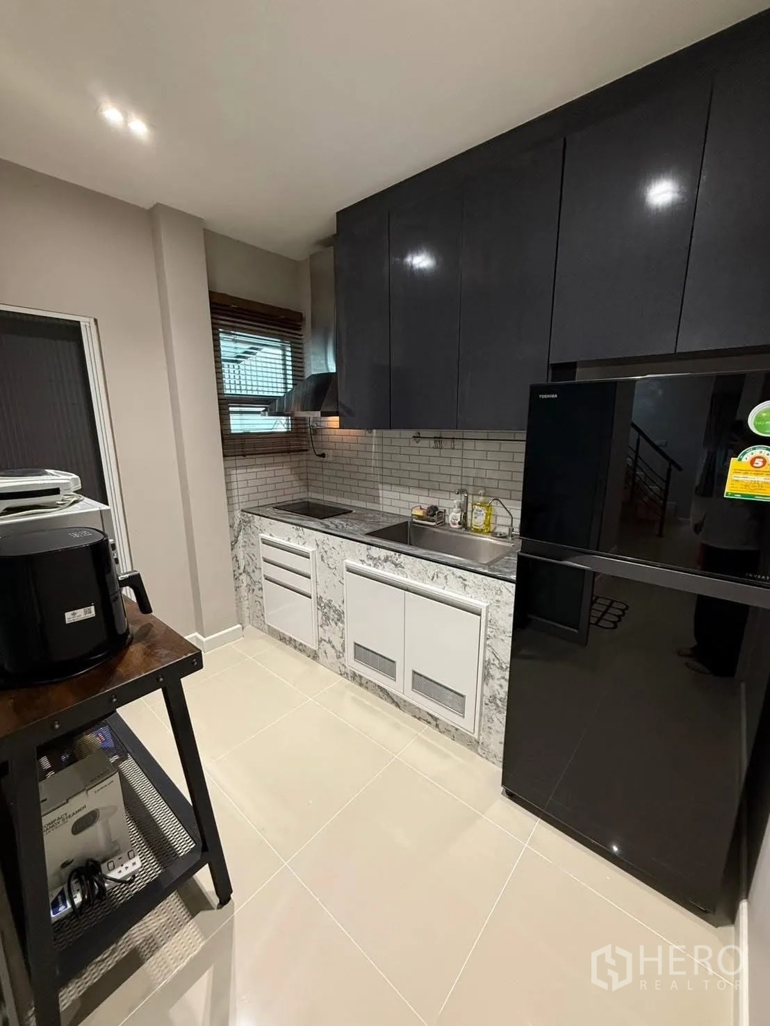 Detached House for rent in Prawet, Bangkok - Kitchen angle with tall black refrigerator, tiled backsplash and built-in cabinets.