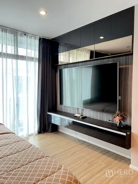 Townhouse for rent in Saphan Sung, Bangkok - Bedroom media wall with mounted big-screen TV, glossy cabinetry and sheer curtains.