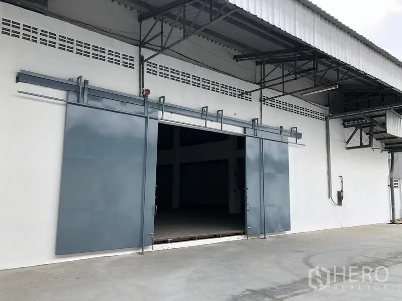 货栈 出租在Nonthaburi - 装卸入口近景，雨棚下的双扇钢制推拉门。
