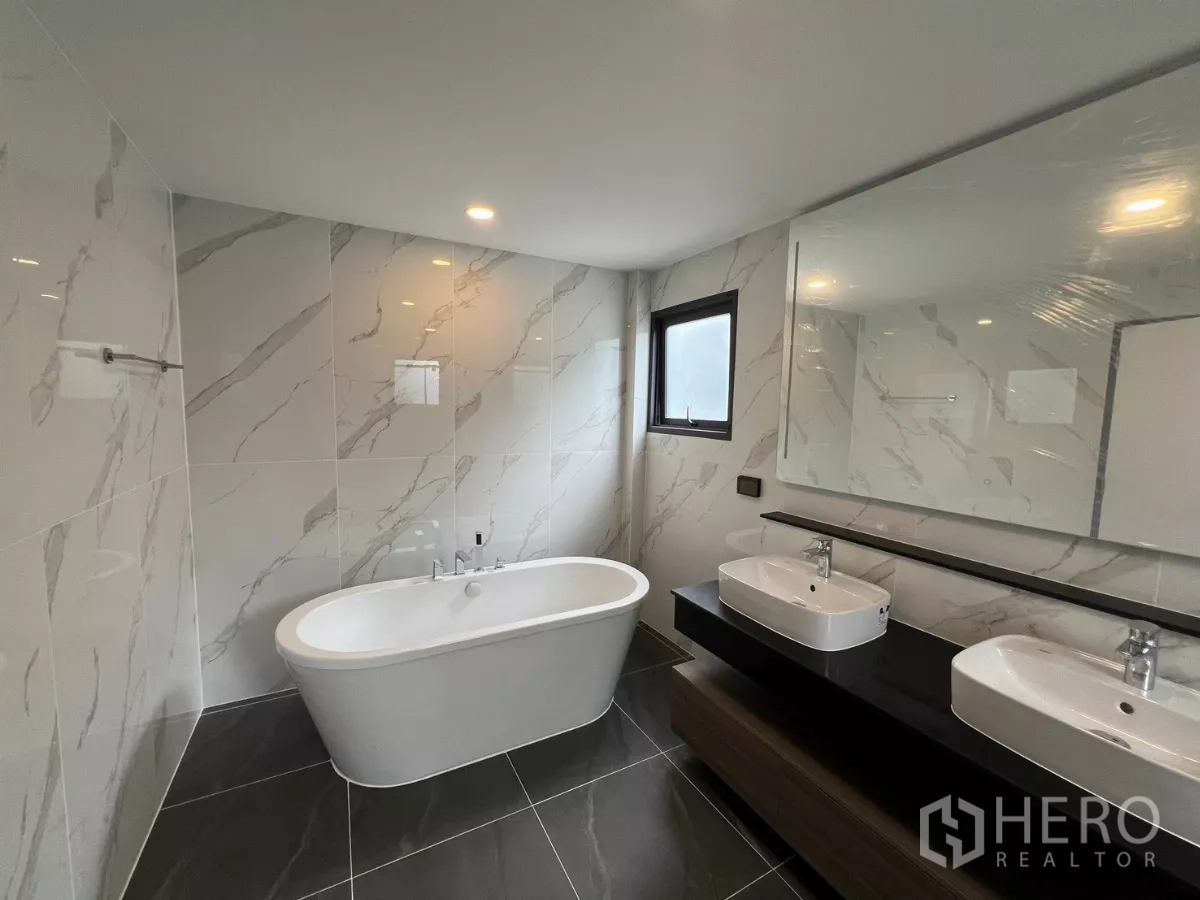 Detached House for rent in Bang Phli, Samut Prakan - Contemporary bathroom with freestanding bathtub, twin basins and marble-effect tiles.