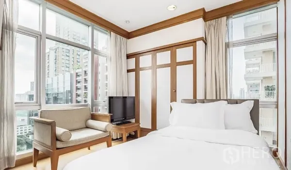 Condominium for rent in Pathum Wan, Bangkok - Second bedroom with floor-to-ceiling windows, built-in wardrobe, TV, and city view.