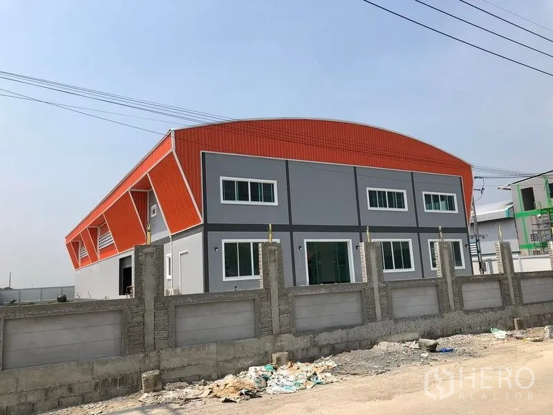 工厂 出售在Mueang Samut Sakhon, Samut Sakhon - 现代两层工厂，橙色弧形屋顶与灰色外立面，前方为混凝土围墙，位于Khok Kham。