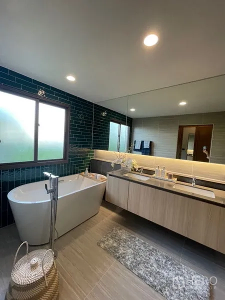 Detached House for sale in Bang Kapi, Bangkok - Contemporary bathroom with freestanding bathtub, double vanity, large mirror and green wall tiles.