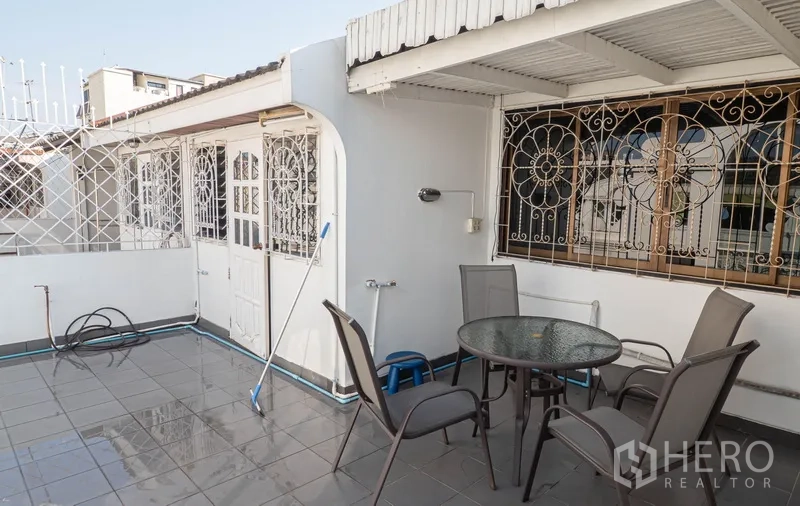 Townhouse for rent in Khlong Toei, Bangkok - Rooftop terrace with tiled floor, outdoor table and metal lattice security.