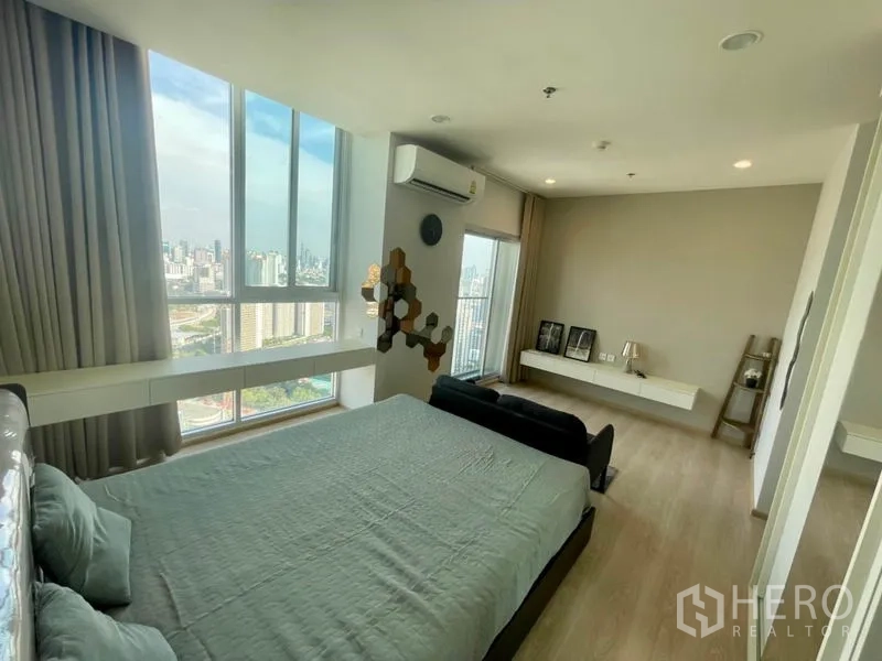 Condominium for rent in Huai Khwang, Bangkok - Corner master bedroom with panoramic city view from tall windows.
