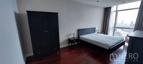 คอนโด ให้เช่าในPathum Wan, Bangkok - ห้องนอนกว้าง พื้นไม้สีเข้ม เตียงและตู้เสื้อผ้าสีดำ พร้อมหน้าต่างบานใหญ่เห็นวิวเมือง ย่านปทุมวัน กรุงเทพฯ