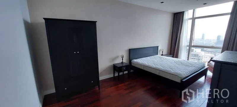 คอนโด ให้เช่าในPathum Wan, Bangkok - ห้องนอนกว้าง พื้นไม้สีเข้ม เตียงและตู้เสื้อผ้าสีดำ พร้อมหน้าต่างบานใหญ่เห็นวิวเมือง ย่านปทุมวัน กรุงเทพฯ