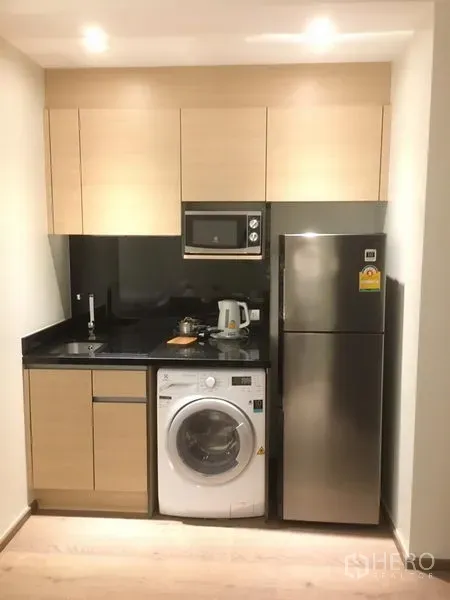 คอนโด ให้เช่าในKhlong Toei, Bangkok - ครัวขนาดกะทัดรัด ตู้ไม้โทนอ่อน เคาน์เตอร์หินสีดำ ไมโครเวฟ เครื่องซักผ้า และตู้เย็นสแตนเลส