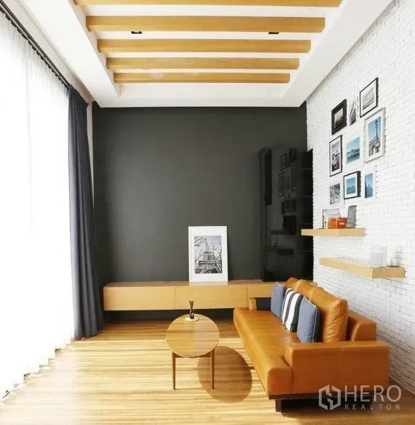 Detached House for rent or sale in Bang Kapi, Bangkok - Cozy family room featuring orange leather sofa, wood flooring, beamed ceiling and display shelves.