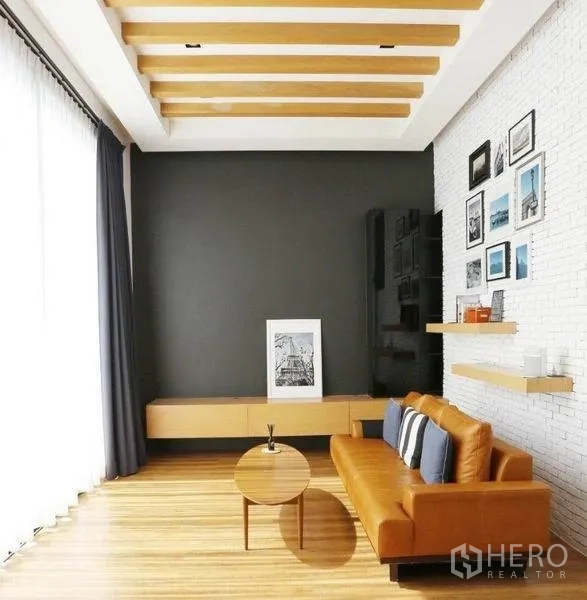 Detached House for rent or sale in Bang Kapi, Bangkok - Cozy family room featuring orange leather sofa, wood flooring, beamed ceiling and display shelves.