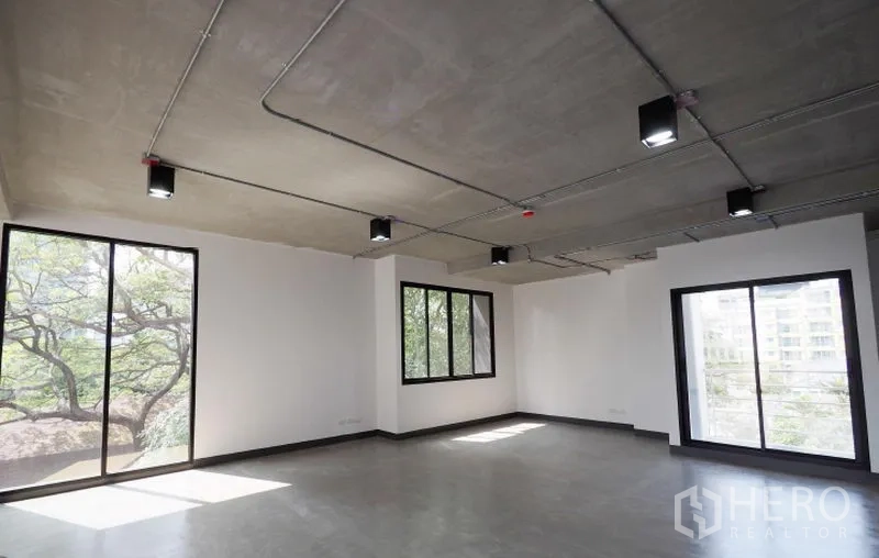 Office Space for rent in Watthana, Bangkok - Bright open-plan Thonglor office with large windows, treetop views, polished concrete floor, and exposed ceiling lights.