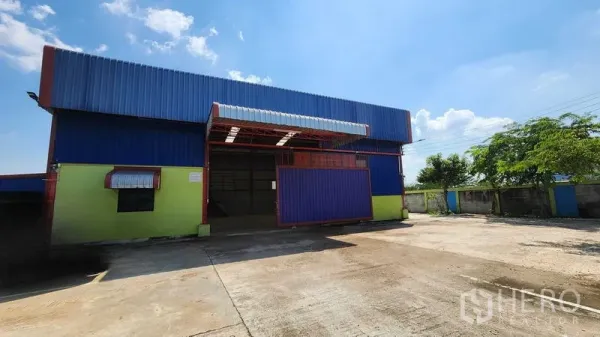 货栈 出租在Nong Chok, Bangkok - 钢板外墙仓库正面，宽幅卷闸门与大面积硬化场地便于卡车进出。