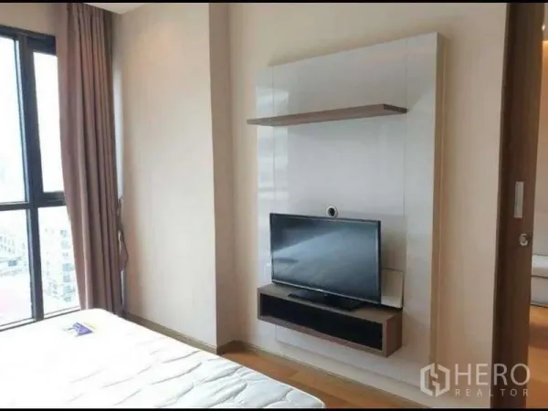 Condominium for rent in Bang Rak, Bangkok - Bedroom corner with wall-mounted TV unit, tall window and curtains in a modern condo.
