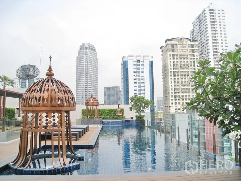 Condominium for rent in Watthana, Bangkok - Rooftop swimming pool with city skyline views, wooden deck, loungers and ornate pavilion structures.