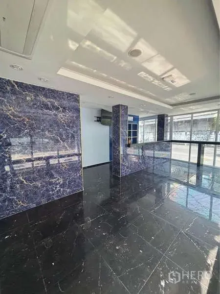 零售空间 出租在Khlong Toei, Bangkok - 开放式销售大厅，黑色亮面大理石地砖与蓝色纹理立柱，采光充足。