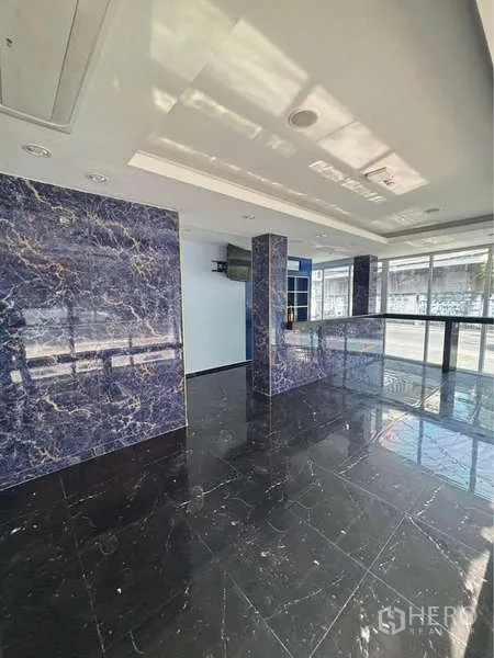 零售空间 出租在Khlong Toei, Bangkok - 开放式销售大厅，黑色亮面大理石地砖与蓝色纹理立柱，采光充足。