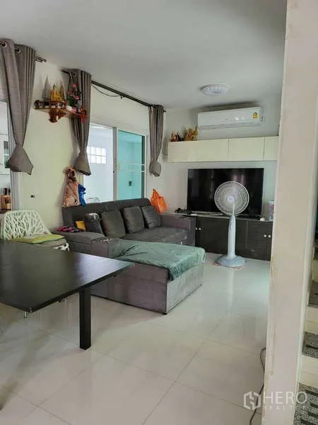 บ้าน ให้เช่าในLat Krabang, Bangkok - ห้องนั่งเล่นอบอุ่น โซฟาเข้ามุม ตู้วางทีวี เครื่องปรับอากาศ และผ้าม่านสูง