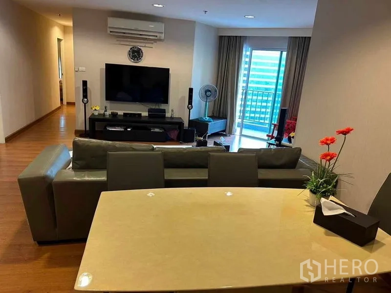 Condominium for sale in Huai Khwang, Bangkok - Living and dining area with TV wall, air conditioner and balcony doors letting in natural light.