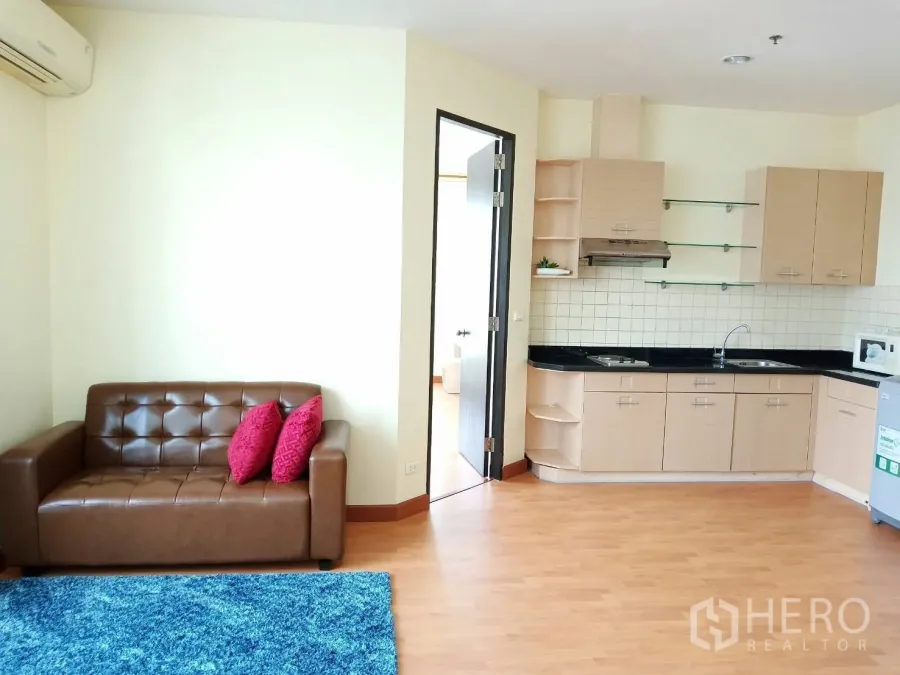 คอนโด ให้เช่าในKhlong Toei, Bangkok - ห้องนั่งเล่นแบบเปิดโล่ง โซฟาหนังสีน้ำตาล พรมสีน้ำเงิน พร้อมครัวบิลท์อินท็อปสีดำและผนังกันเปื้อนกระเบื้อง