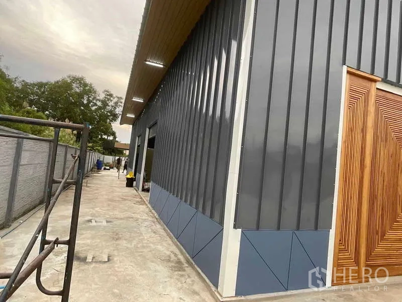 คลังสินค้า ให้เช่าหรือขายในNong Chok, Bangkok - มุมด้านข้างโกดังผนังเมทัลชีทพร้อมไฟส่องสว่างและประตูไม้ ทางเดินคอนกรีต