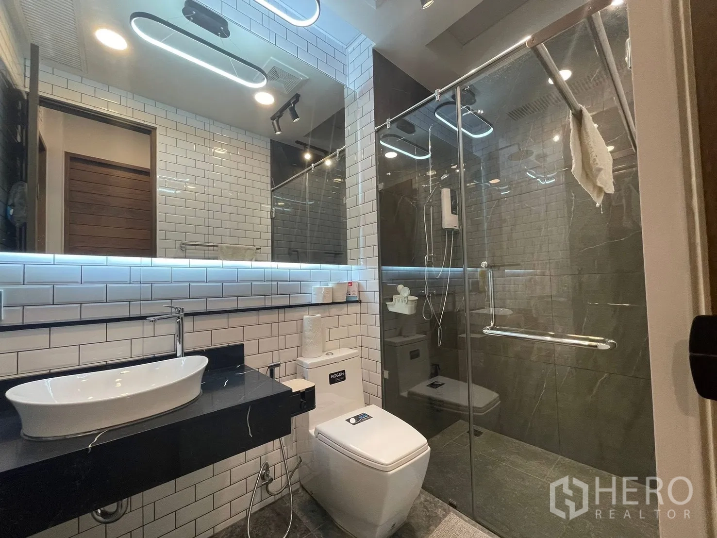 Home Office for rent or sale in Bang Kapi, Bangkok - Renovated bathroom featuring glass-enclosed shower, subway tile walls and backlit mirror.
